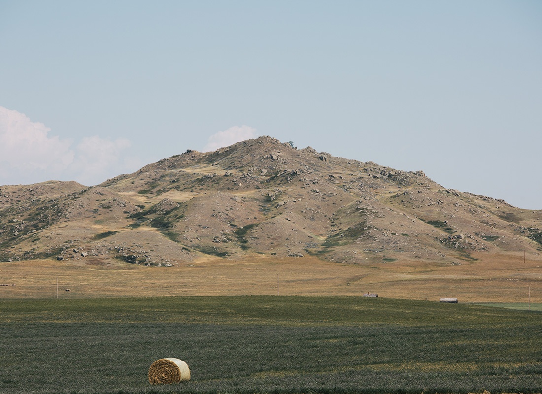 Beach, ND - View of a Sandy Mountain Next to a Field of Rolled Hay on a Sunny Day on a Farm in North Dakota