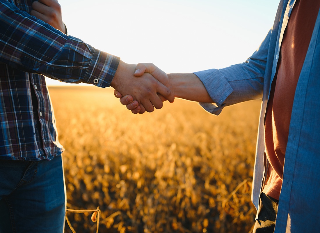 Our Business Partners - Closeup View of Two Farmers Shaking Hands While Standing on a Farm Field at Sunset