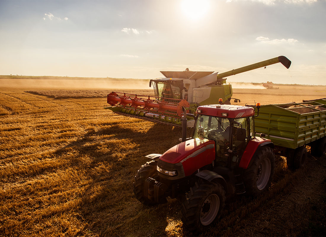 Revenue Protection Insurance - View of a Harvesting Tractor and Combine Harvesting Wheat on a Field at Sunset